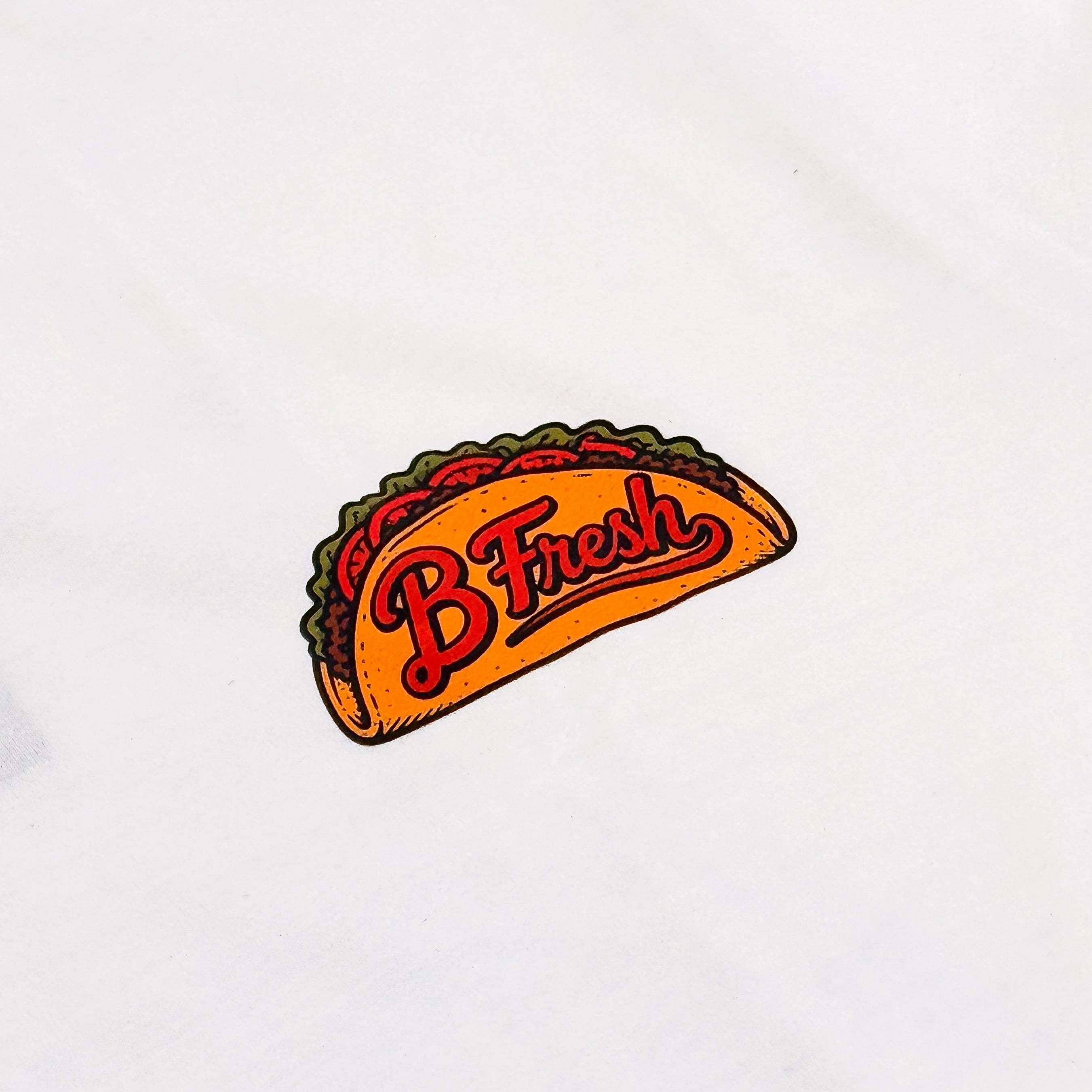 A close-up of a taco patch with the word 'B Fresh' in red script.