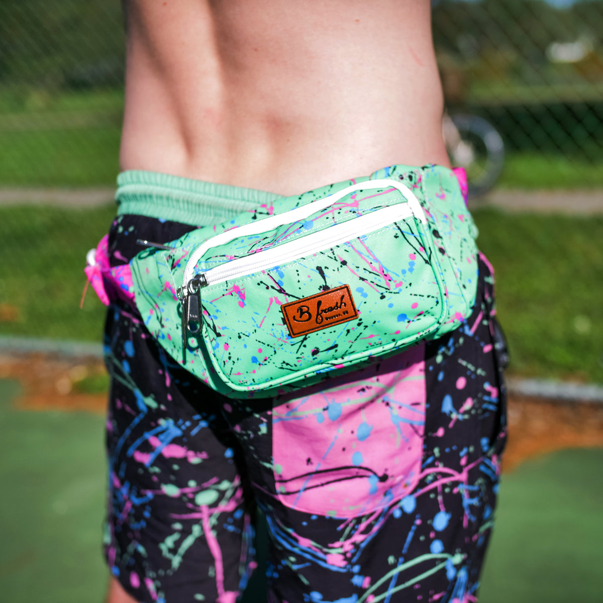 Man wearing retro B Fresh Gear splatter 90s green blue black pink fanny pack bum bag. B Fresh Gear.